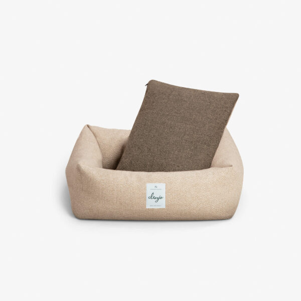 Rektangulär hundbädd med textiletikett framtill. I hundbädden står en mörkbrun kudde.
